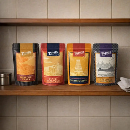 Four Patang snacks with colorful labels on a wooden shelf against a tiled wall.