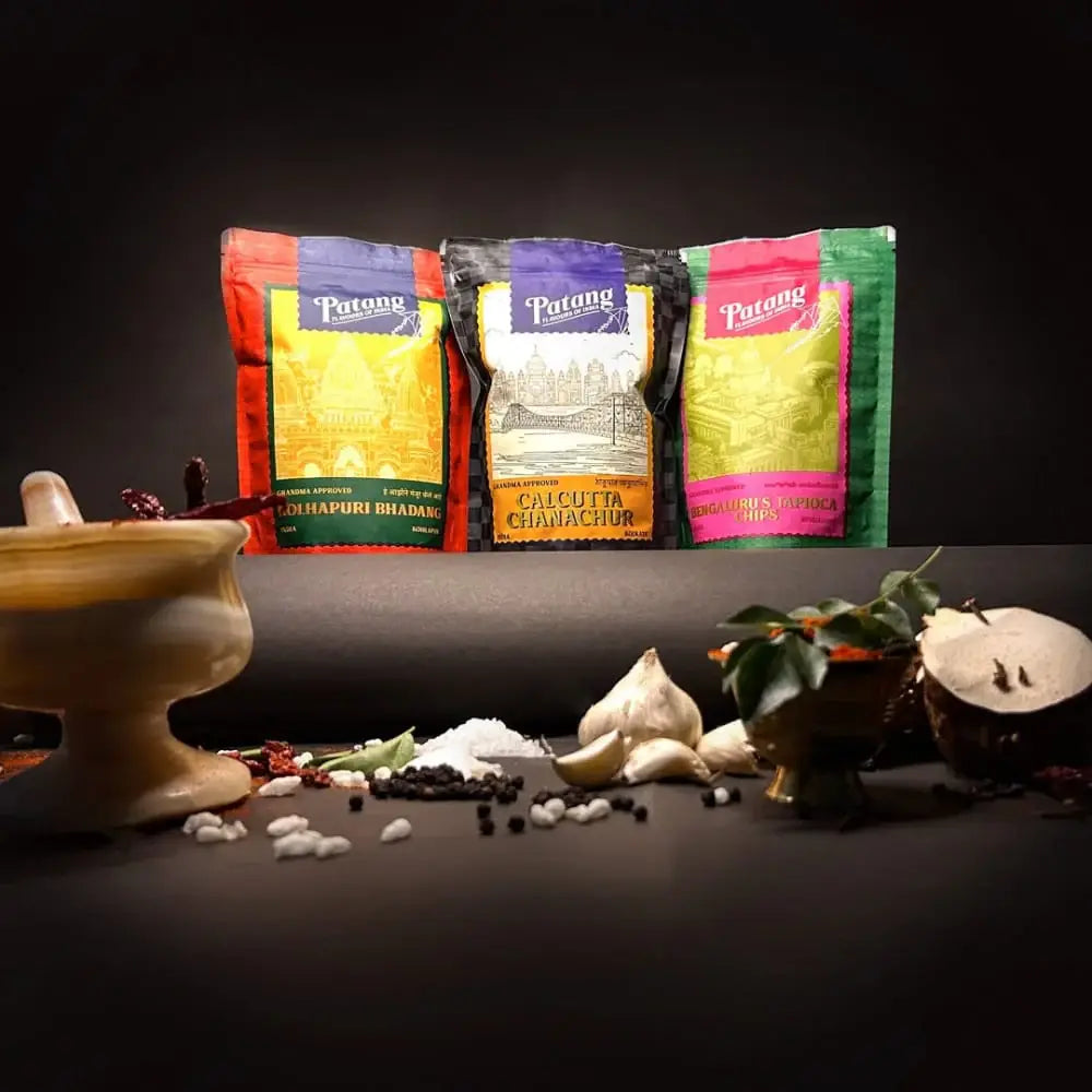 Three Patang spice packages with spices and a mortar and pestle on a dark background.