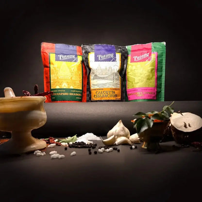 Three Patang spice packages with spices and a mortar and pestle on a dark background.