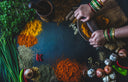 Person grinding spices with a mortar and pestle on a table surrounded by various herbs and spices.