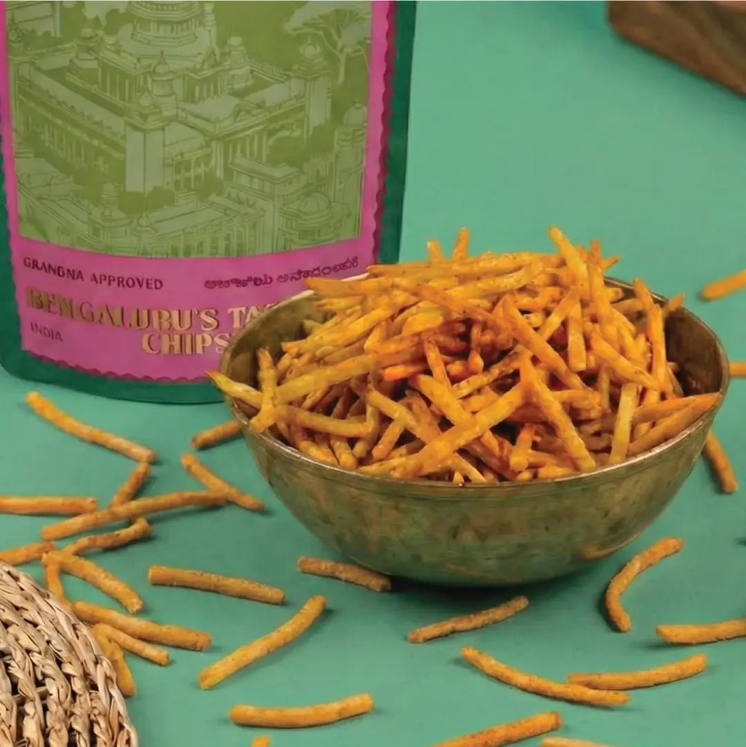 Bowl of chips with a packaging box labeled Bengaluru's Tapioca Chips on a teal background