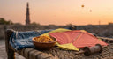 Bowl of snacks, red and yellow kites, and string spool on a woven bed with a tower in the background